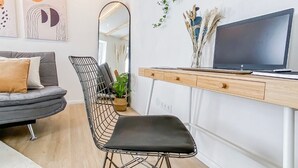 Un salon moderne avec un canapé gris, un fauteuil noir, un bureau en bois avec une télévision et un miroir.