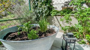 Un grand bac à fleurs en métal contenant diverses plantes, une petite lanterne en métal et une clôture en treillis métallique, le tout dans un jardin.