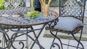 Une terrasse extérieure avec une table ronde en métal, deux chaises et une bouteille de vin.