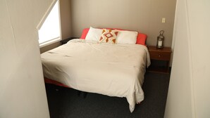A neatly made bed with a white and red bedspread, a small bedside table with a lantern, and a window providing natural light. - NEW - Private Downtown Christiansted Apartment (Christiansted)