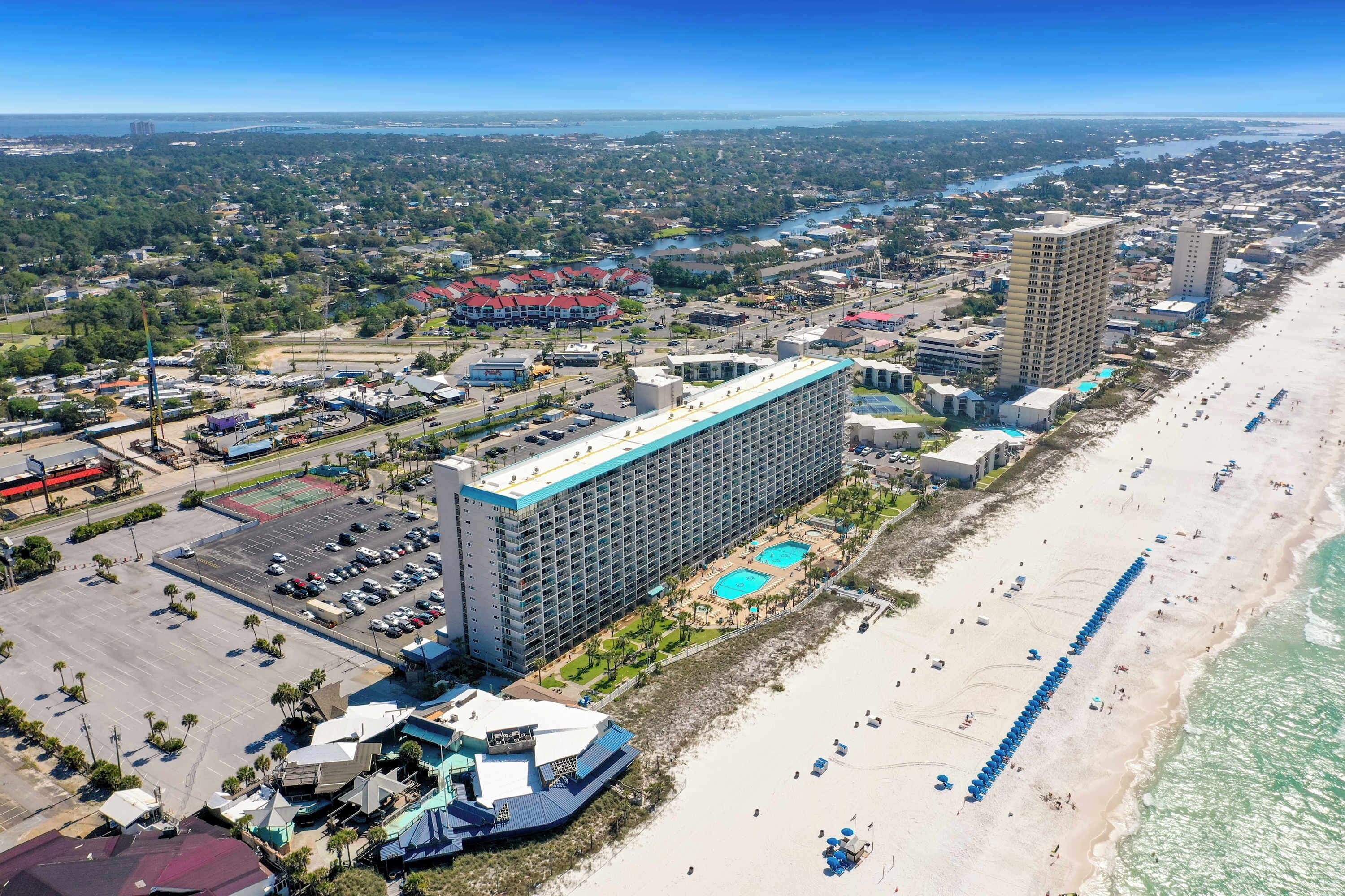 A coastal hotel with a large building, a swimming pool, and a beach area.