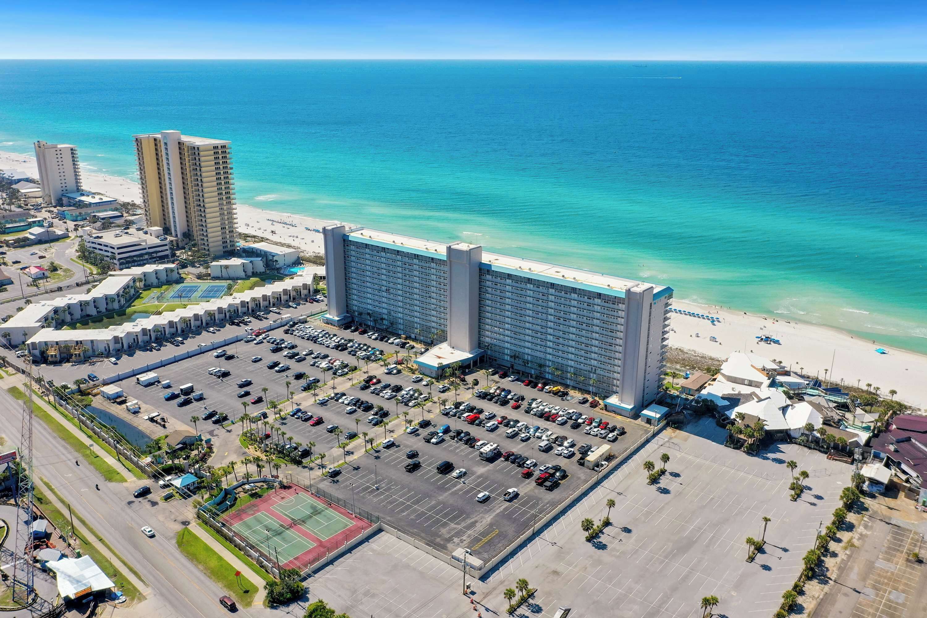 Un grand hôtel composé de plusieurs immeubles de grande hauteur, avec un parking et une plage en arrière-plan.
