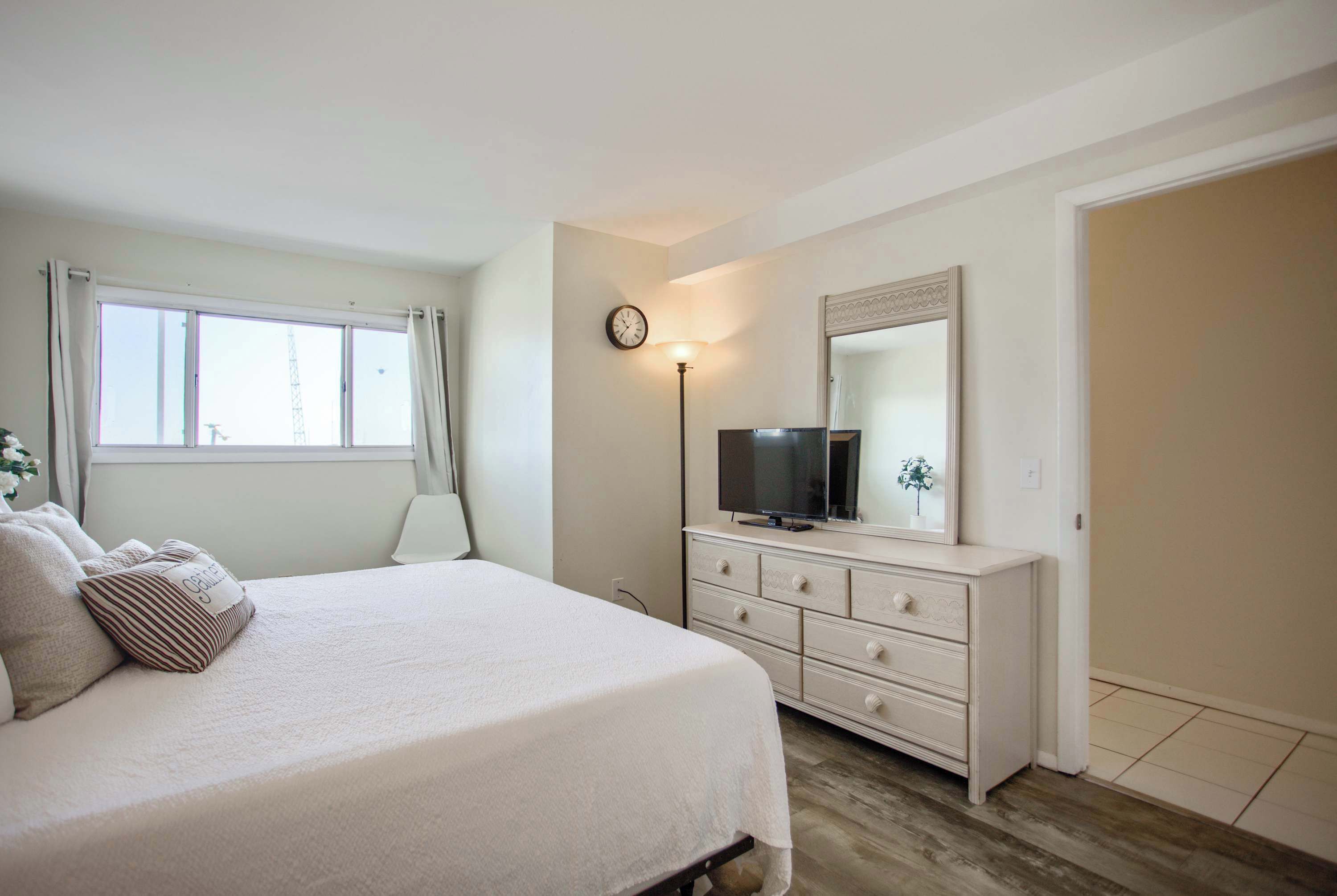 A bedroom with a bed, a dresser, a television, and a clock on the wall.