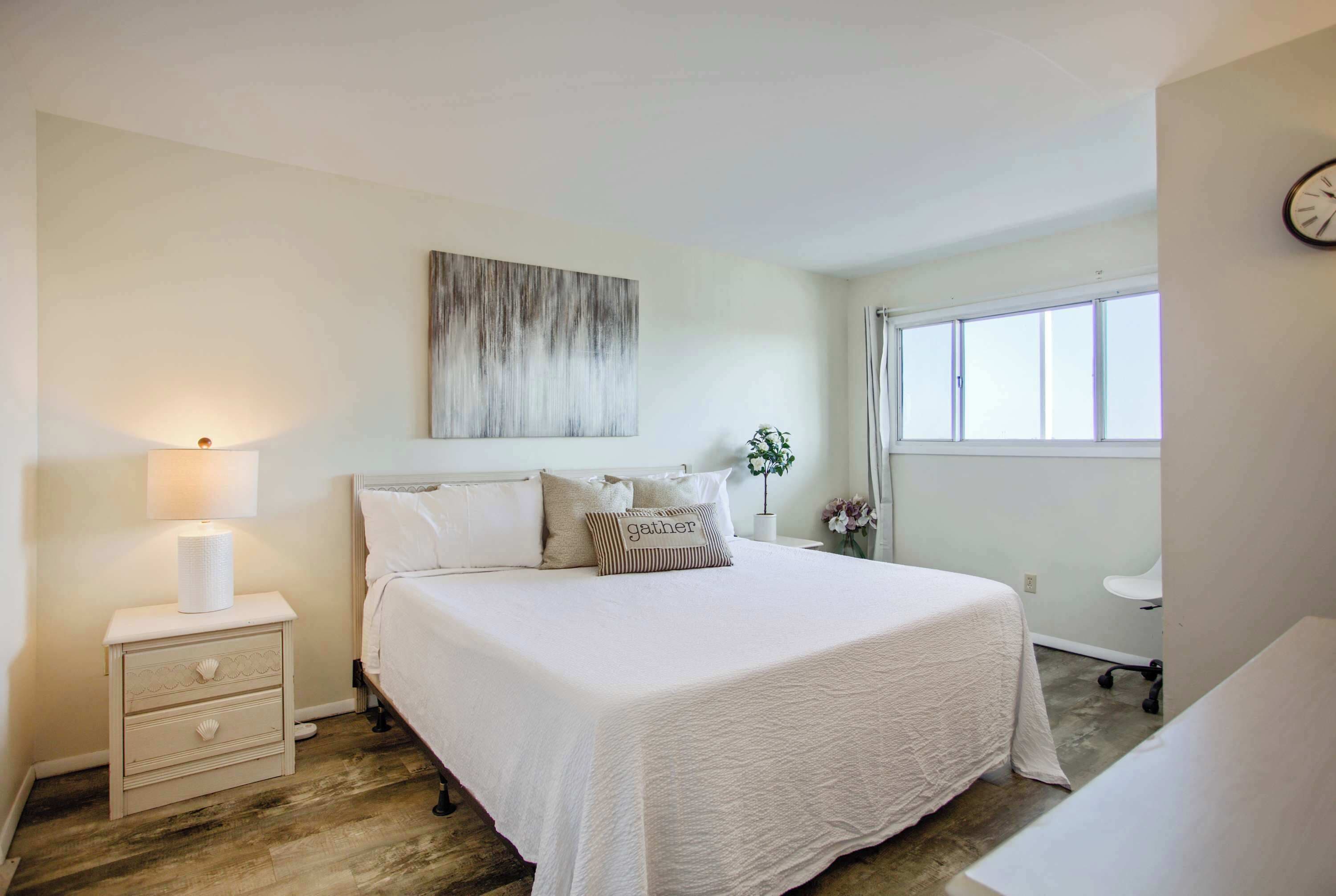 A neatly arranged bedroom with a large bed, a bedside table with a lamp, and a window with curtains.