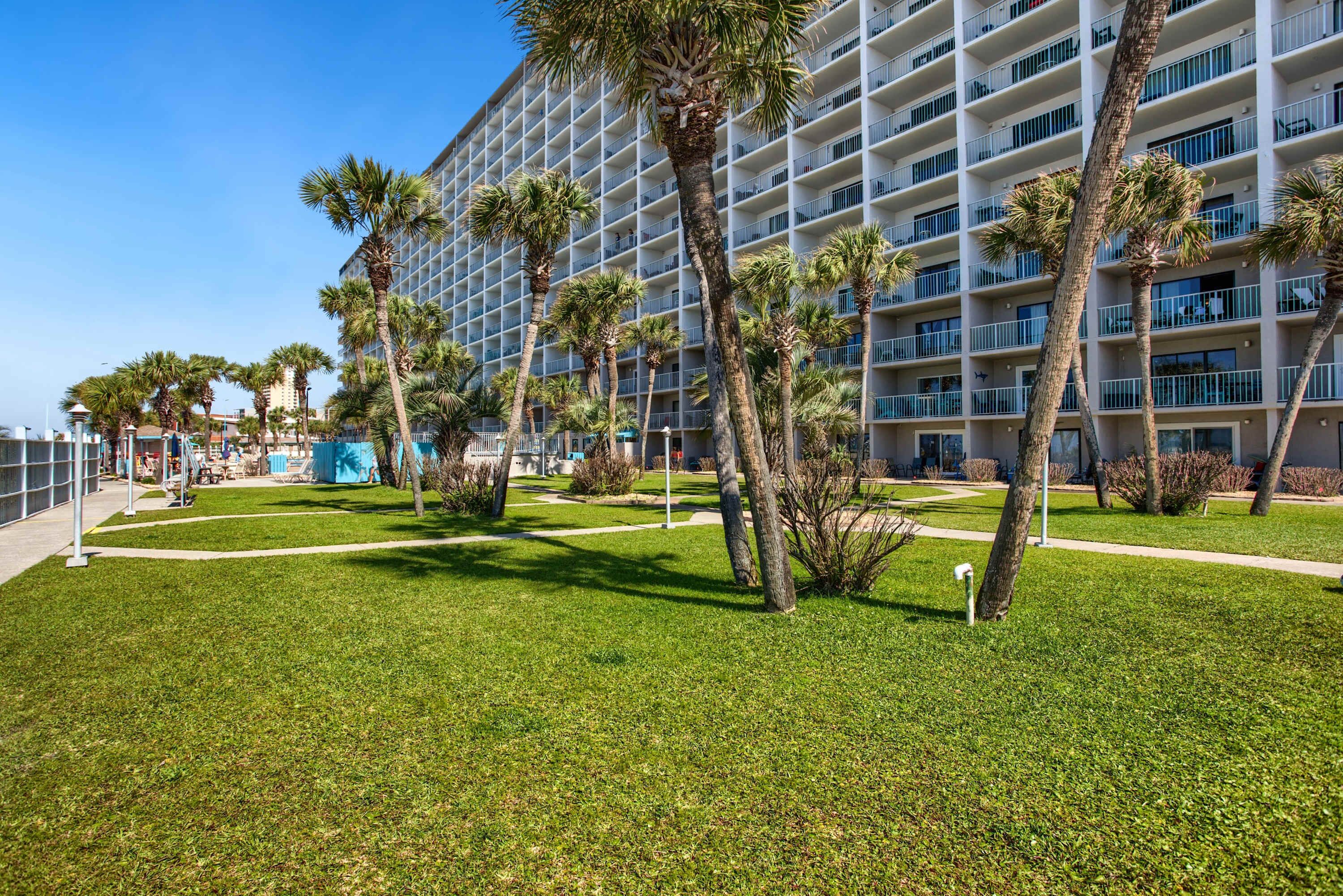 A hotel with a modern design, featuring a large building with multiple balconies and palm trees in the courtyard.