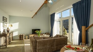 Ein Wohnzimmer mit einer Couch, einem Esstisch mit Tellern und Gläsern, einem Fernseher und einem Fenster mit Vorhängen.