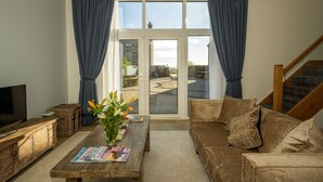Ein Wohnzimmer mit einer Couch, einem Couchtisch mit Zeitschriften, einem Fernseher und Blick durch eine Glastür.