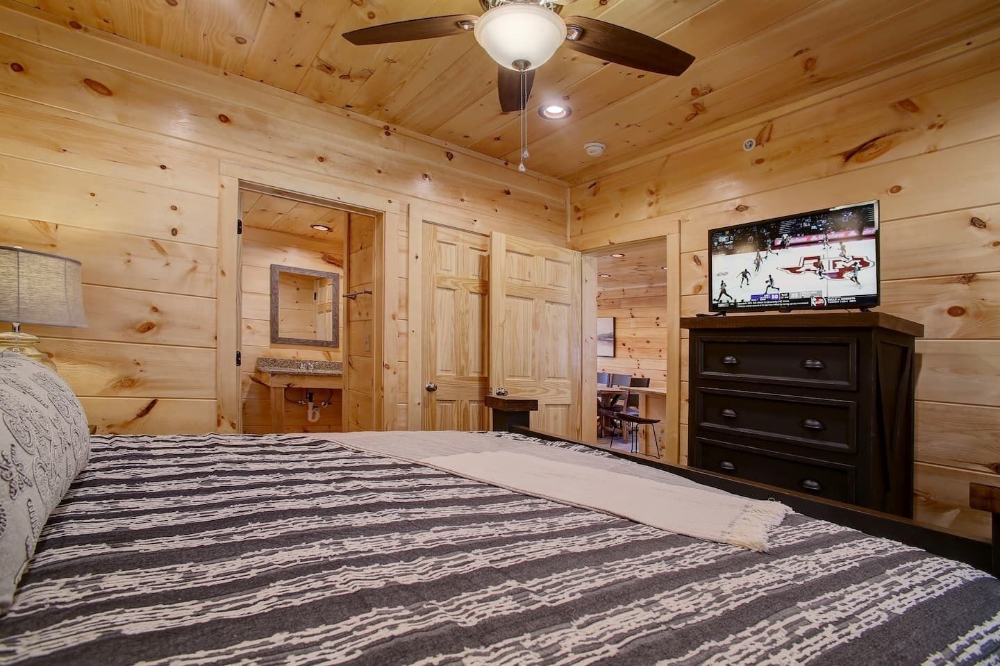 Camera da letto in una baita di legno con letto, cassettiera, televisore e ventilatore a soffitto.