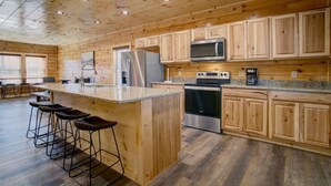 Cocina con gabinetes de madera, refrigerador de acero inoxidable, microondas, horno y encimera de granito.