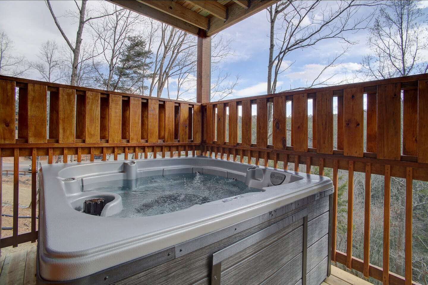 A hot tub under a wooden deck with a view of trees.