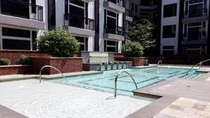 Piscina com superfície de água cristalina, rodeada por uma parede de tijolos e um deck revestido de azulejos.