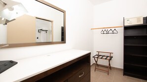 A bathroom with a large mirror, a white countertop, a wooden vanity, and a towel rack with towels.