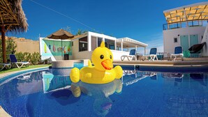 A swimming pool with a yellow inflatable duck, lounge chairs, and a building with a mural.
