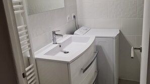 A small bathroom with a white sink, mirror, and a compact washing machine.