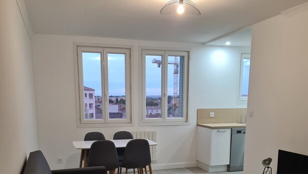 A modern living room with a sofa, coffee table, and dining area. There are large windows with a city view.