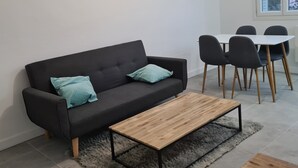 A modern living room with a black sofa, two teal cushions, a wooden coffee table, and a grey furry rug.