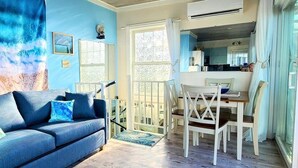 A living room with a blue sofa, a dining area with a table and chairs, and a view of the kitchen through an open door.