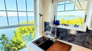 A kitchen with a large window overlooking a body of water and trees.