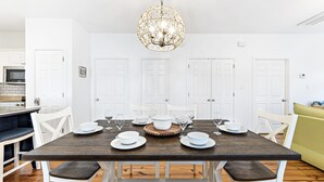 A dining area with a wooden table set for six, white chairs, and a decorative light fixture above.