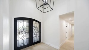 Un couloir avec une porte en verre à cadre noir, un luminaire au plafond de forme géométrique et un plancher en bois.