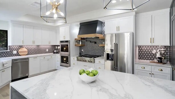Une cuisine moderne avec des meubles blancs, un plan de travail en marbre, des appareils électroménagers en acier inoxydable et un luminaire décoratif au plafond.