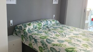 A bedroom with a bed, a nightstand, a drawer, and a wall-mounted light switch. - Beach apartment (Salou)