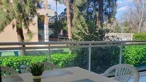 A terrace with a table and chairs, surrounded by greenery and a view of a building. - Beach apartment (Salou)