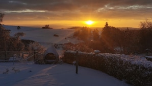 Eine verschneite Landschaft bei Sonnenuntergang, ein eingezäuntes Gelände und ein kleines Gebäude.