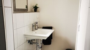 Ein kleines Badezimmer mit Toilette und Waschbecken, über dem Waschbecken befindet sich ein Spiegel, und auf einem Regal steht ein kleiner Topfpflanze.