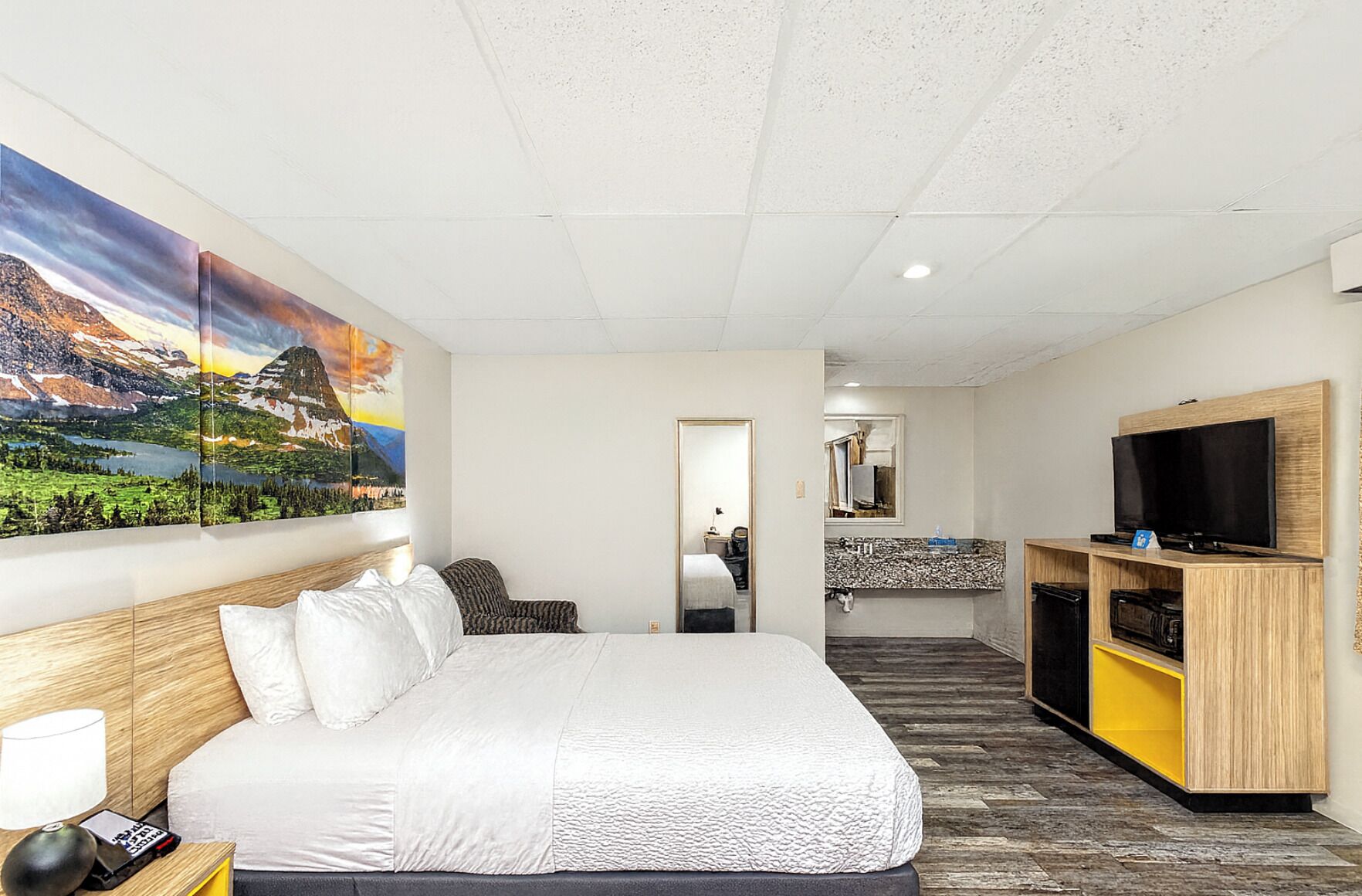 Habitación de hotel con una cama grande, televisión, una kitchenette y un baño visible a través de una puerta abierta.