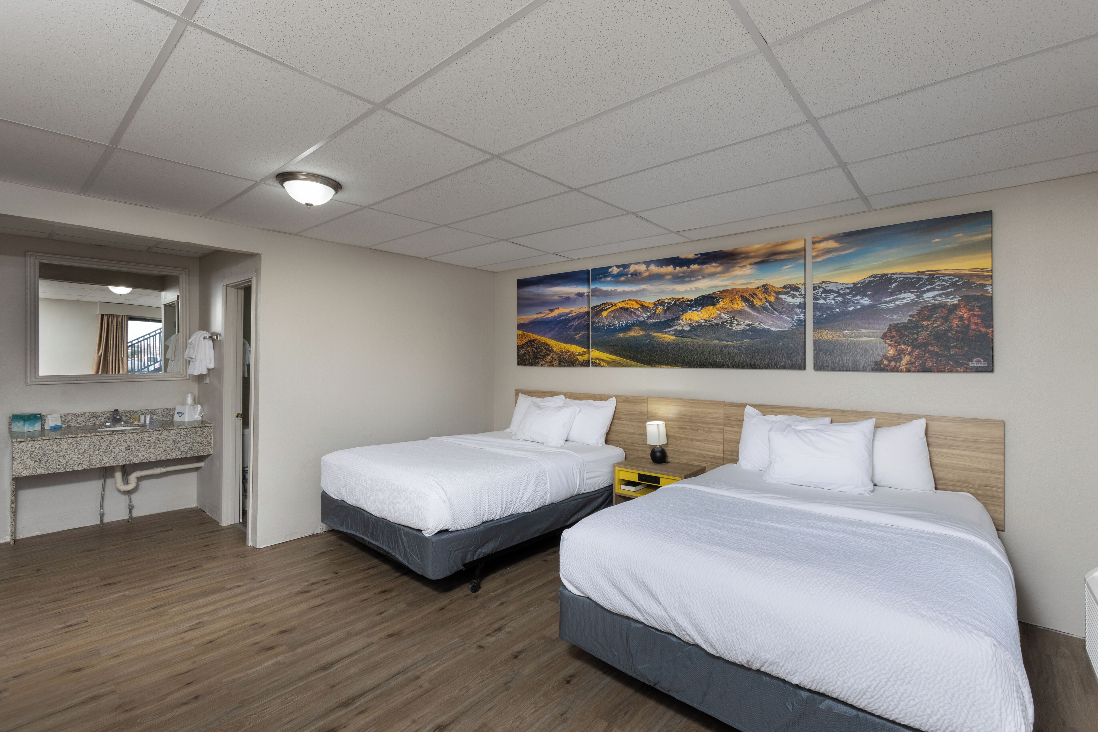 Ein Hotelzimmer mit zwei Betten, einem Badezimmer mit Waschbecken und einem großen Landschaftsbild an der Wand.