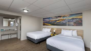 Ein Hotelzimmer mit zwei Betten, einem Badezimmer mit Waschbecken und einem großen Landschaftsbild an der Wand.