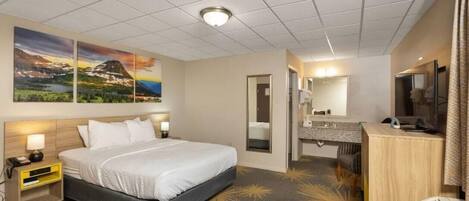 Une chambre d’hôtel avec un lit, un bureau, un miroir et des œuvres d’art accrochées au mur.