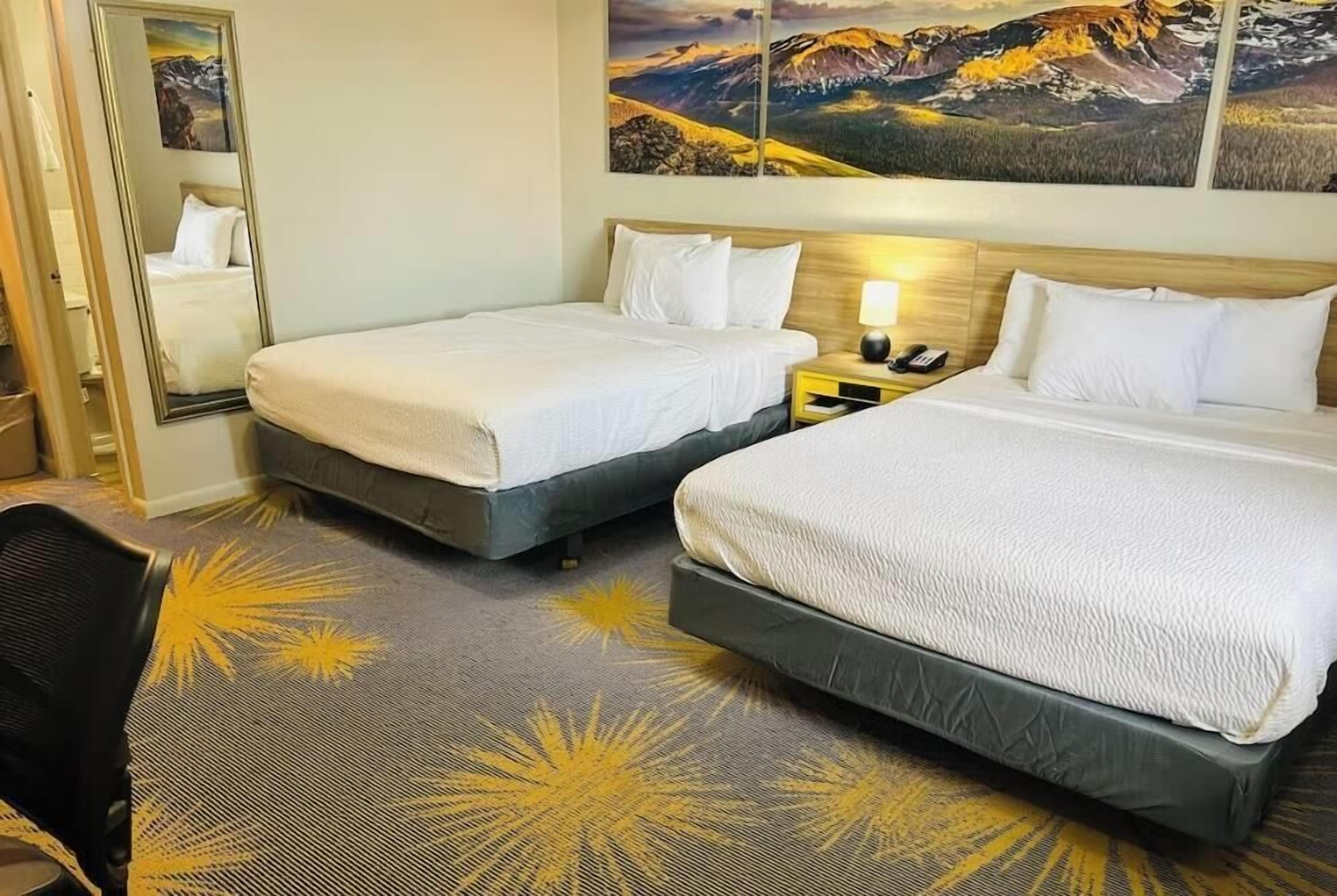 A hotel room with two beds, a nightstand with a lamp, a mirror, and a carpet with a mountain landscape design.