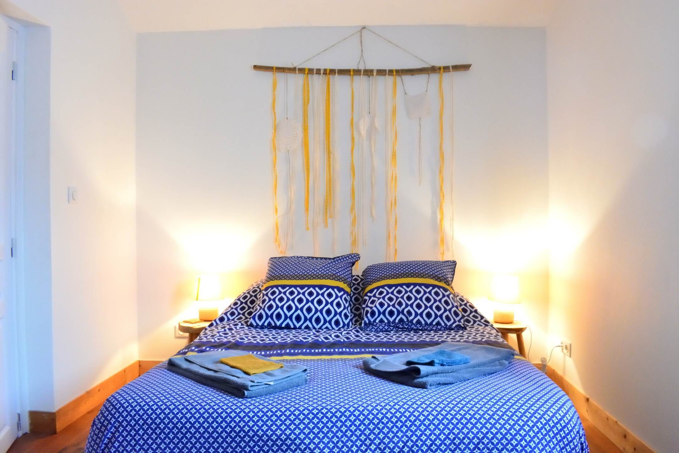 Une chambre à coucher avec un lit, des coussins à motifs, une décoration suspendue et des lampes de chevet.