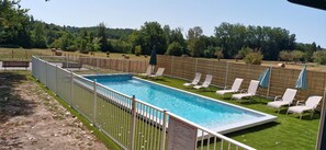 Piscina rectangular con cerramiento blanco, rodeada de césped y árboles.