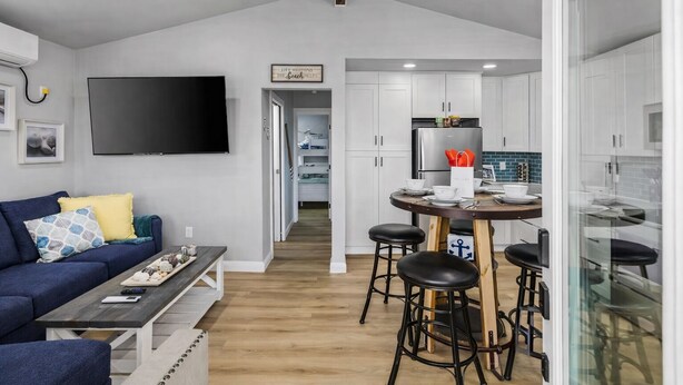 A modern kitchen with white cabinets, a stainless steel refrigerator, and a dining area with a wooden table and bar stools.