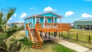 A turquoise house with a wooden deck and a staircase leading to a porch.