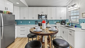 A modern kitchen with white cabinets, a stainless steel refrigerator, a wooden dining table with four chairs, and a blue-tiled backsplash.
