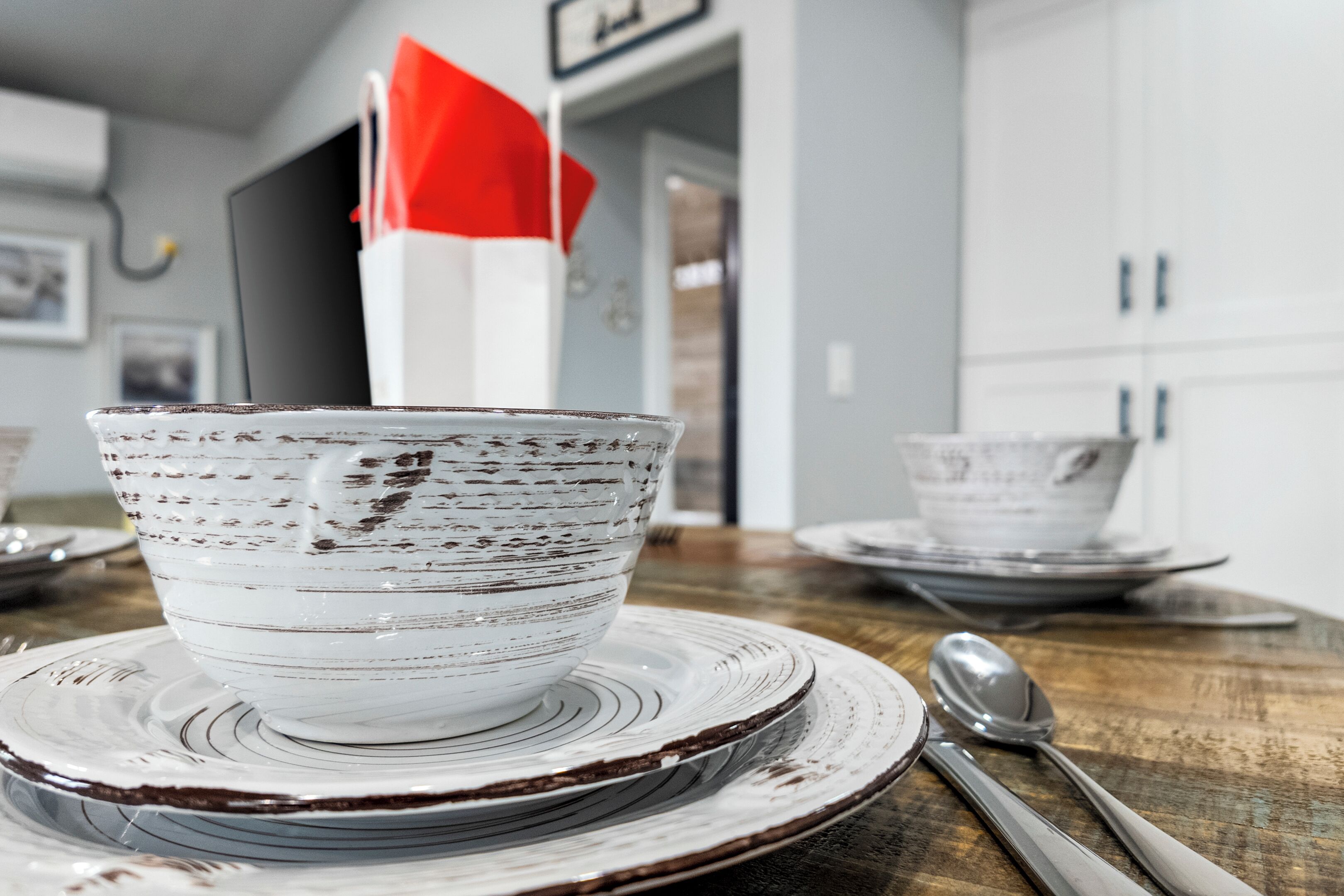 A kitchen with white cabinets, a wooden table, and a white bowl with a red napkin on it.