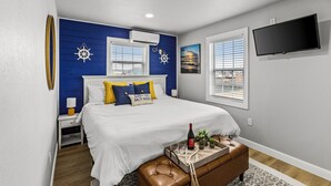 A bedroom with a bed, a TV, a window, and a wall-mounted air conditioner.
