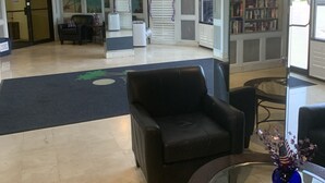 En entréhall med en receptionsdisk, svarta läderfåtöljer, ett glasbord med en vas, en bokhylla och en takfläkt.