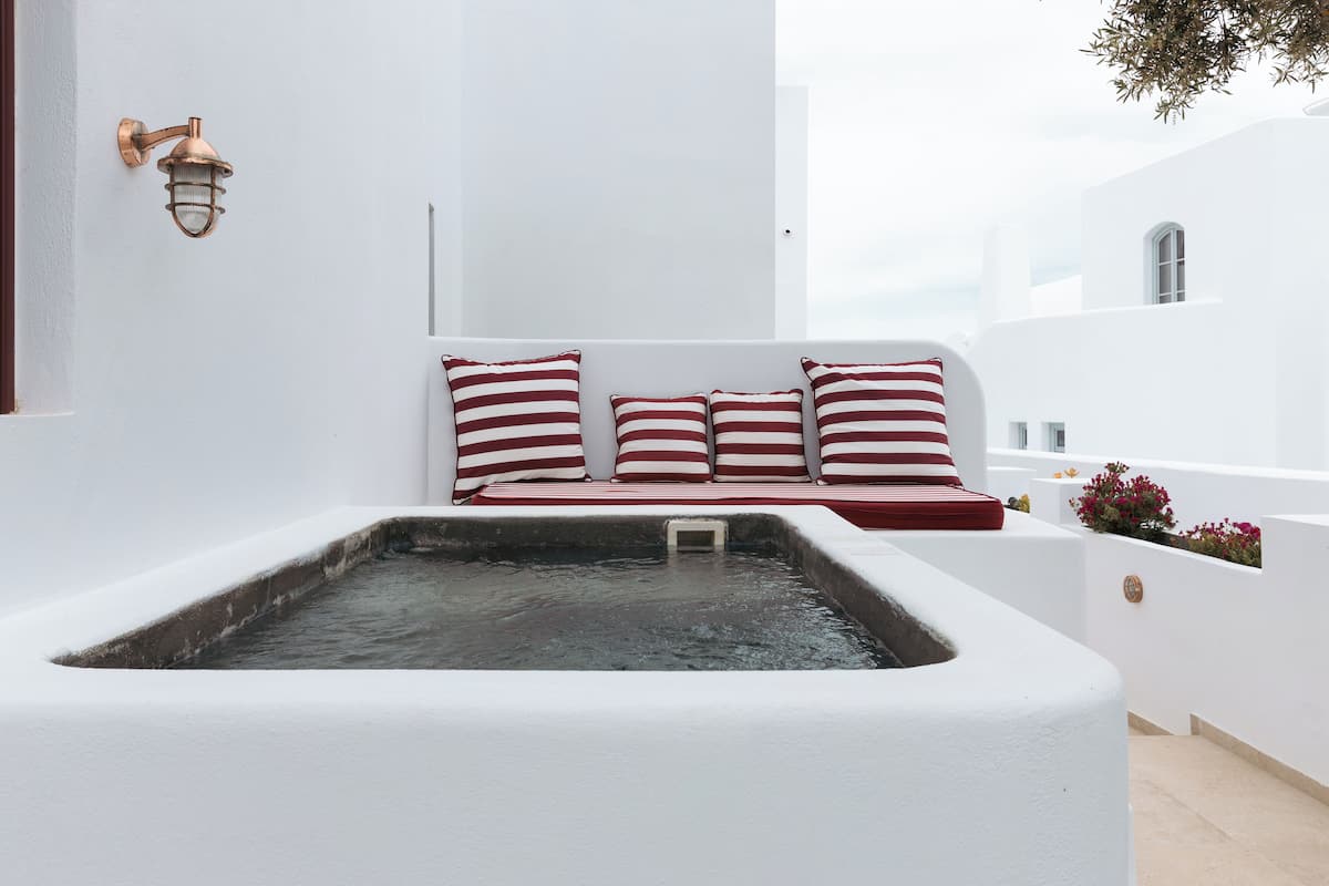 Un espace extérieur aménagé avec des sièges blancs, un jacuzzi, des coussins à rayures rouges et blanches, et un luminaire fixé au mur.