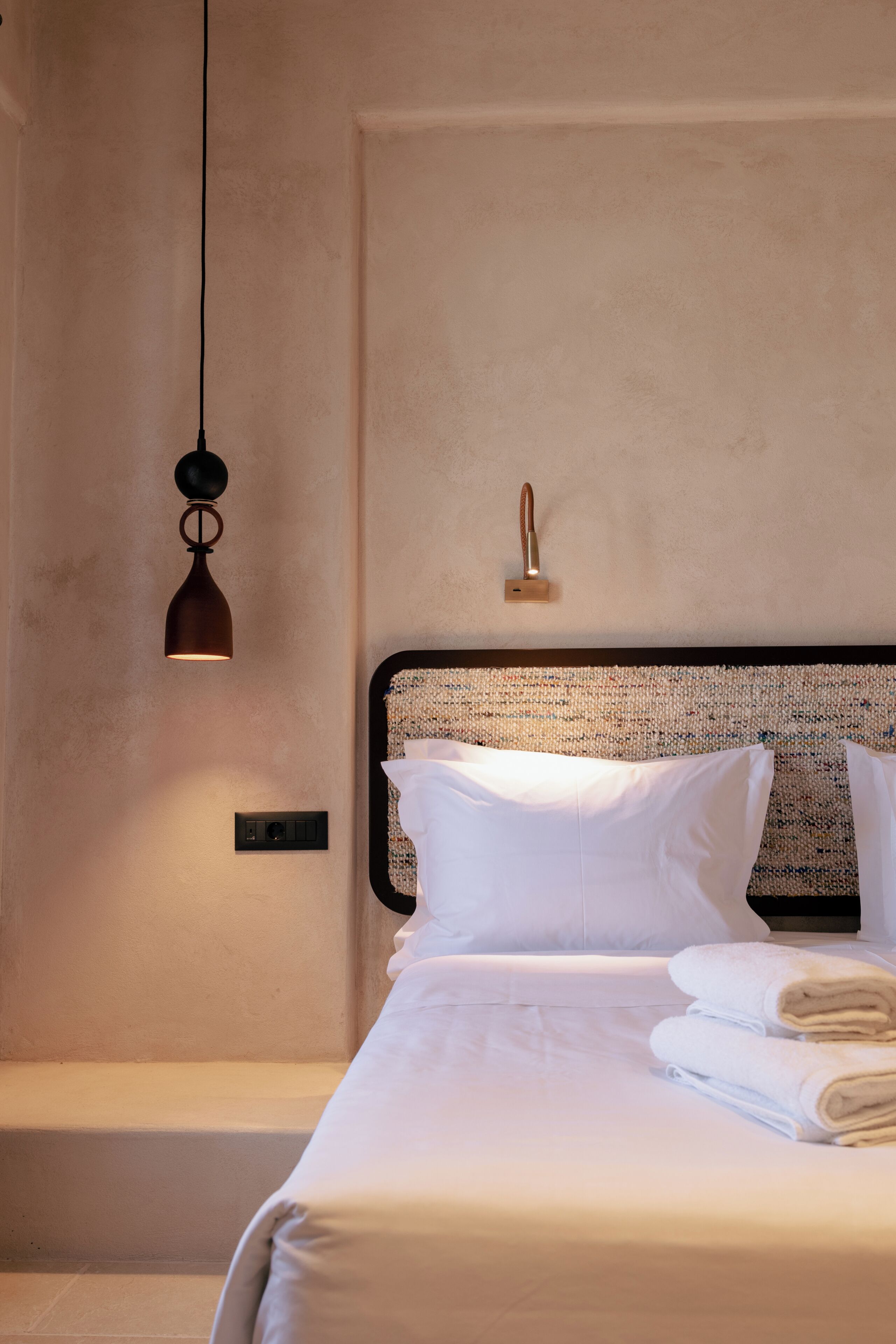 Un lit bien fait, avec du linge de lit blanc, une tête de lit à motifs et un luminaire suspendu.