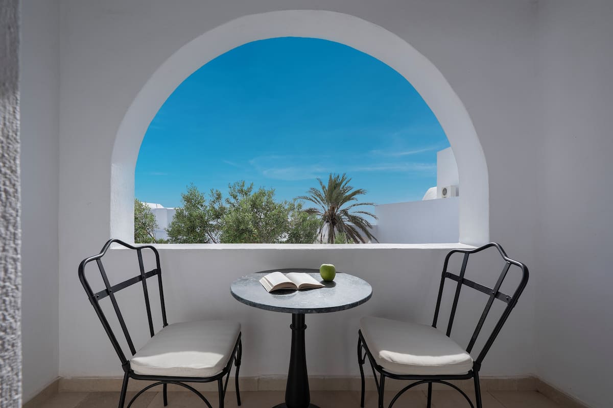 Un balcon avec deux chaises et une petite table ronde, un livre et une pomme verte.