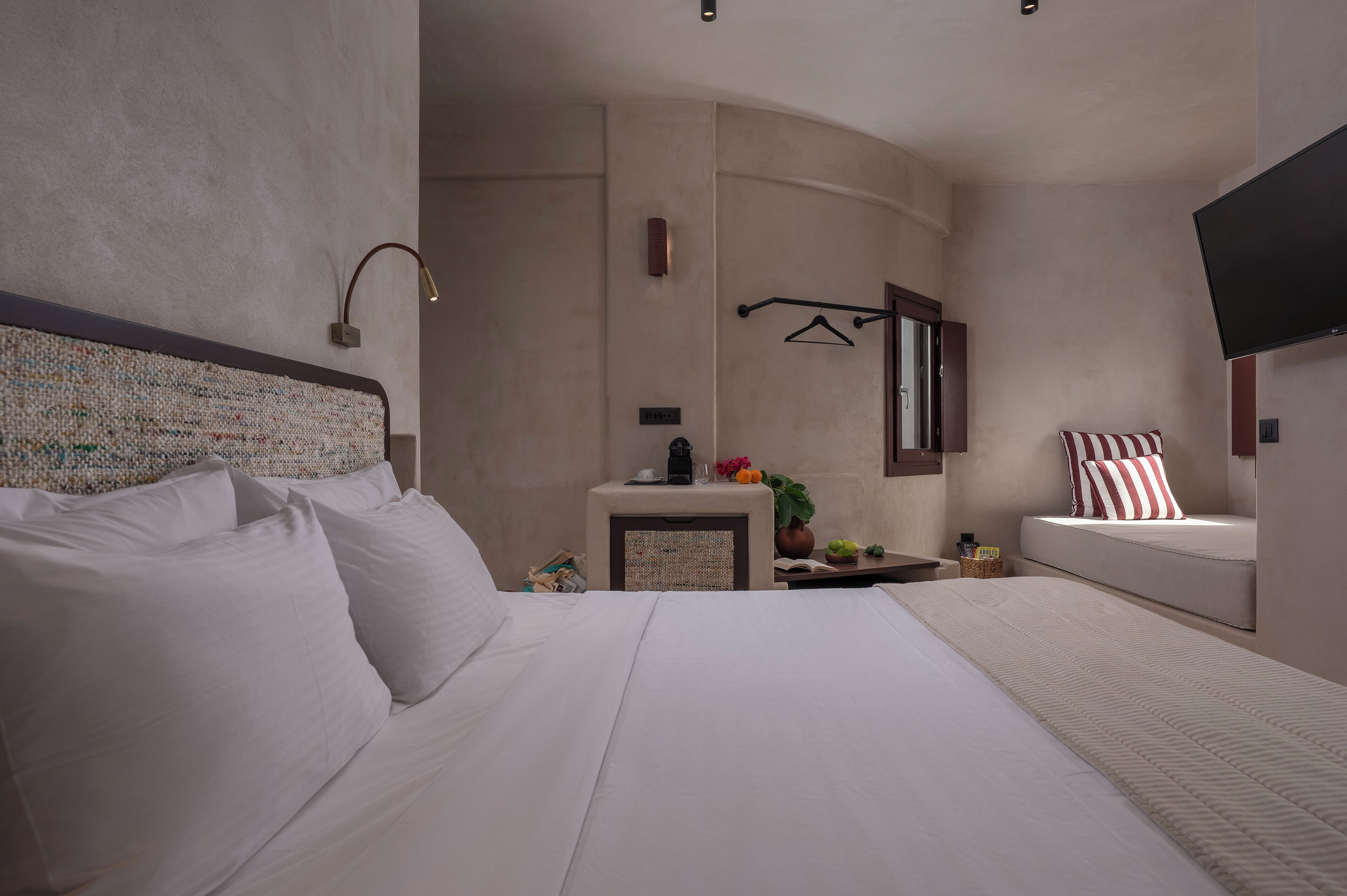 A hotel room with a large bed, a bedside table, a small table with a plant, a TV mounted on the wall, and a hanging light fixture.