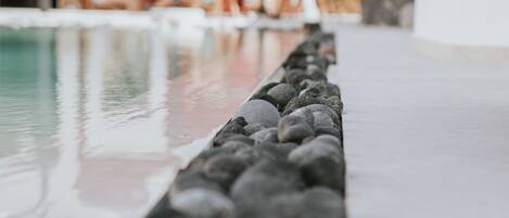 Uima-allas, jonka reunat on koristeltu pienillä kivillä, punainen seinä ja taustalla ulkotila, jossa on istuimia.
