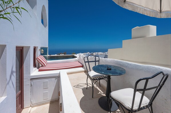 A rooftop terrace with a view of the sea, a small table, chairs, and a red and white striped cushion.