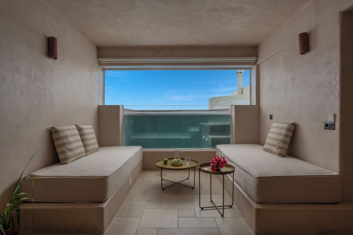 Un balcon avec deux canapés de couleur beige, une petite table ronde ornée d’un vase, et une vue sur la mer.