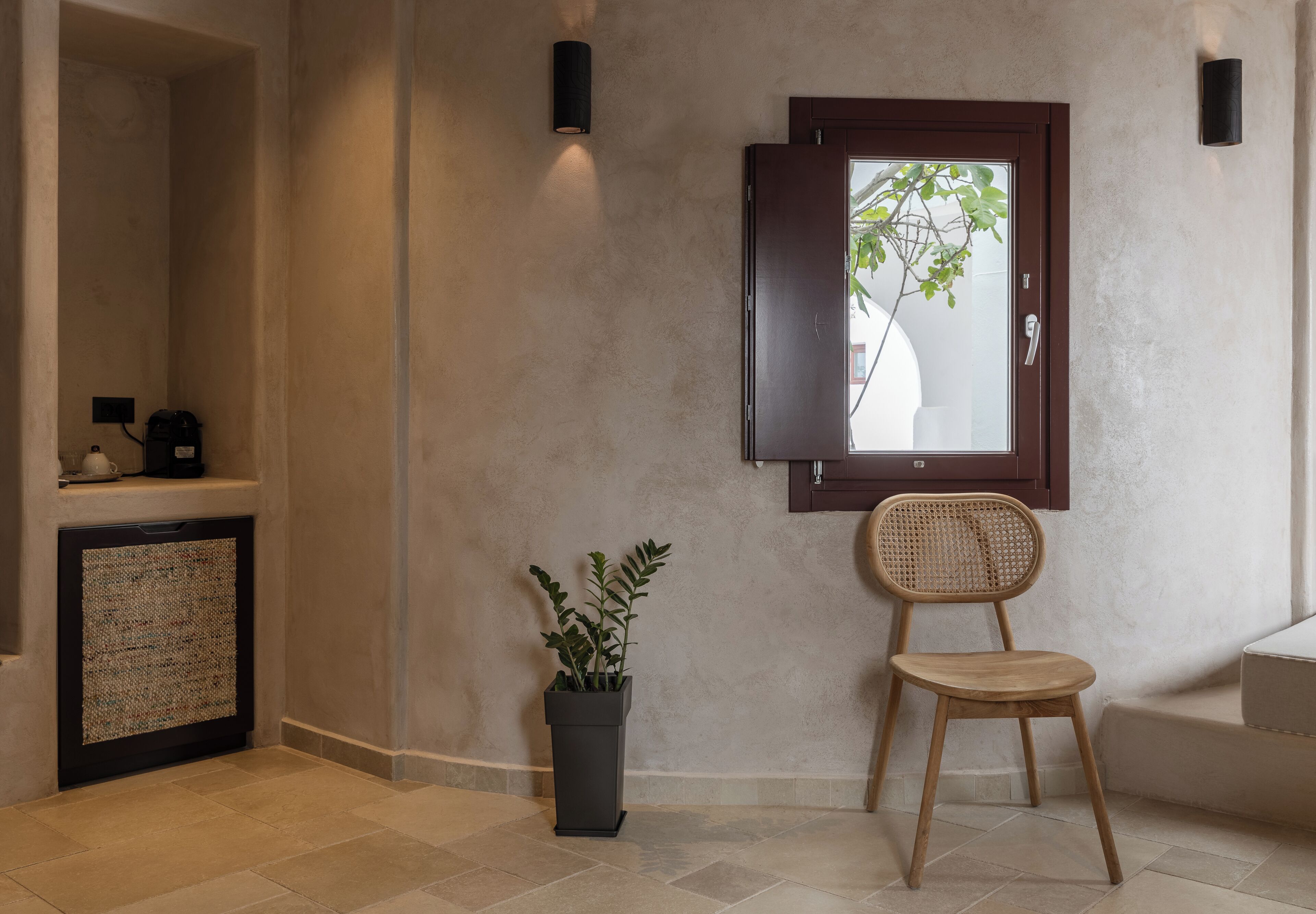 A room with a wooden chair, a potted plant, a window with a view, and a shelf with items.